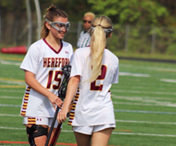 Eleni Yates (left) and Mackenzie Moroney (‘25) (right) wish each other luck with a stick-high-five before a game.