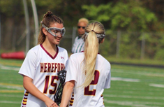 Eleni Yates (left) and Mackenzie Moroney (‘25) (right) wish each other luck with a stick-high-five before a game.
