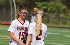 Eleni Yates (left) and Mackenzie Moroney (‘25) (right) wish each other luck with a stick-high-five before a game.  