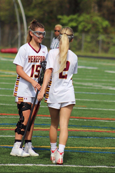 Eleni Yates (left) and Mackenzie Moroney (‘25) (right) wish each other luck with a stick-high-five before a game.  